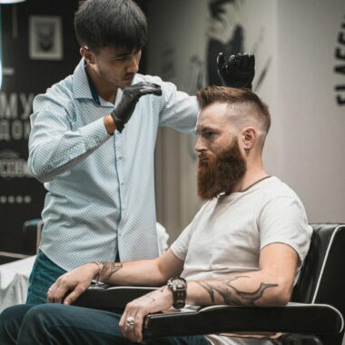 A barber expertly styles a bearded man's hair in a modern barbershop setting.