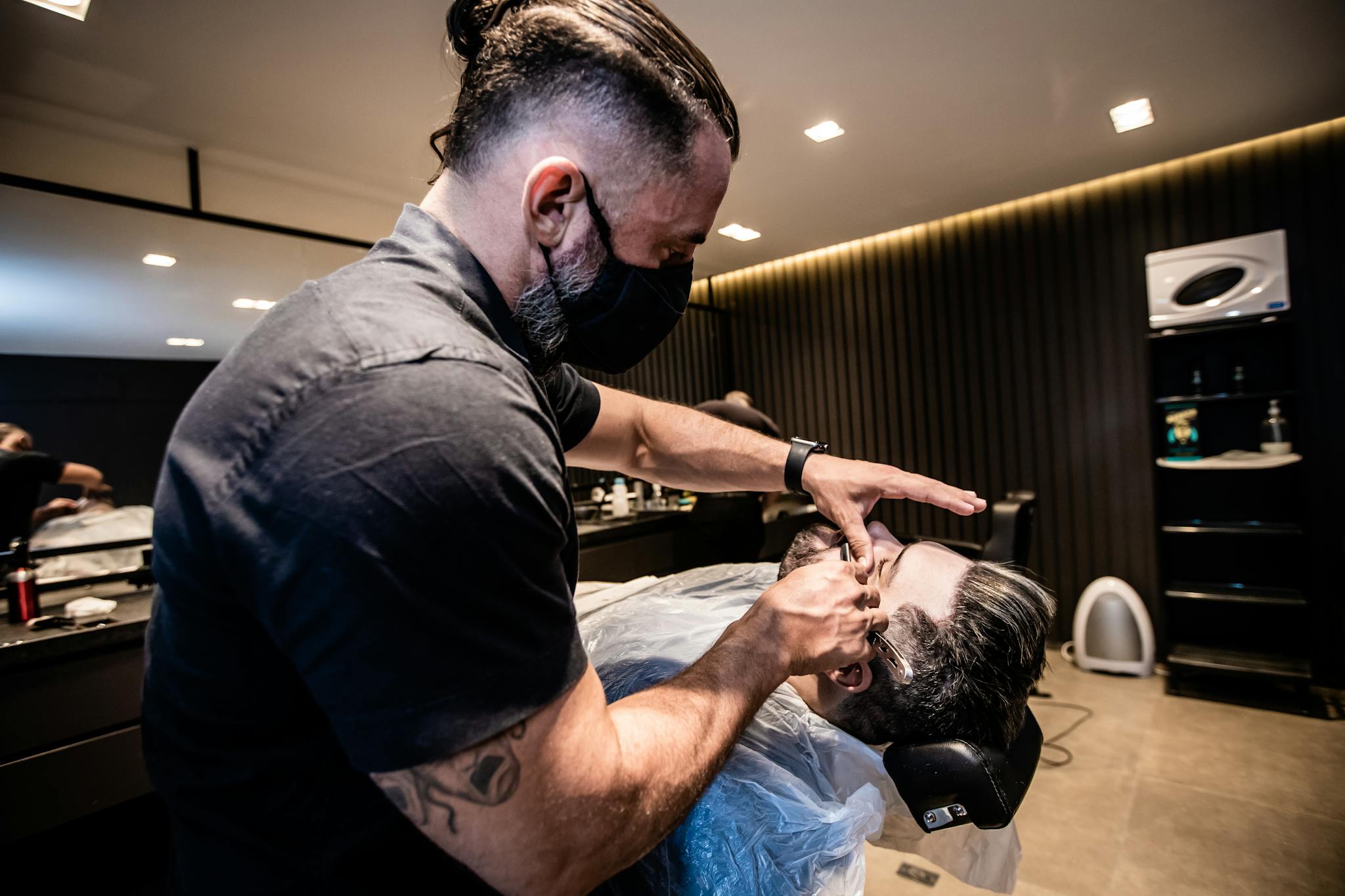 Barber expertly shaves client using straight razor in stylish salon. Captured indoors, showcasing modern grooming.