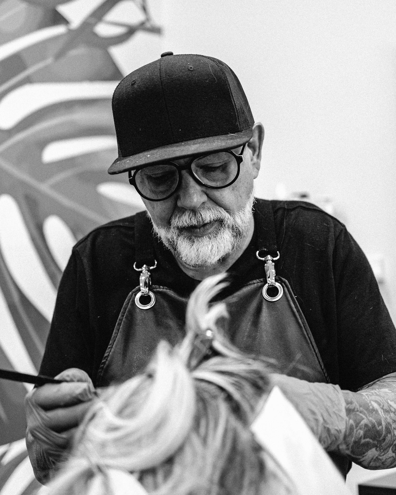 Black and white portrait of a hairdresser styling a client's hair in a salon setting.