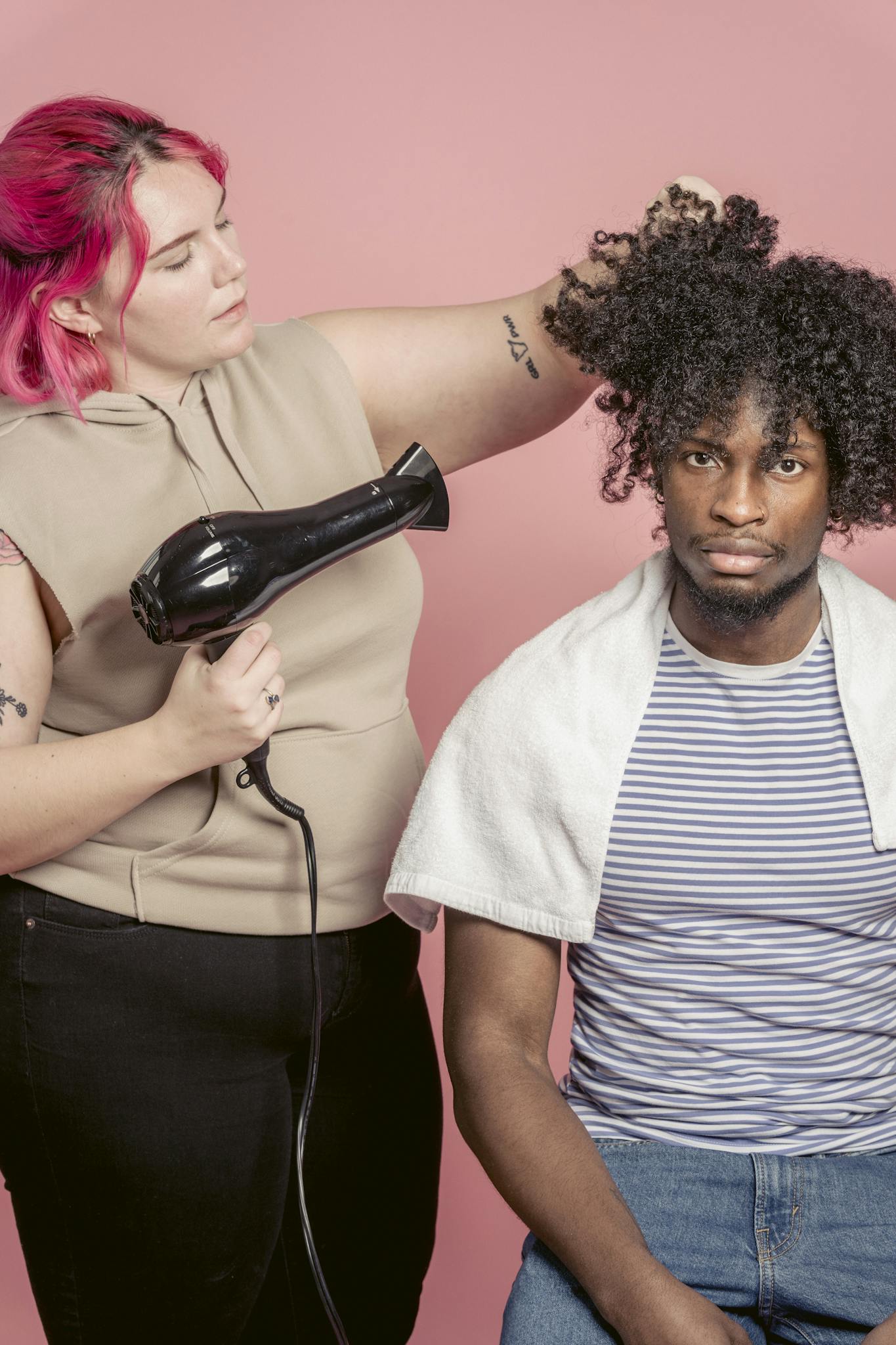 Hairdresser uses a dryer to style a client's curly hair in a studio setting.