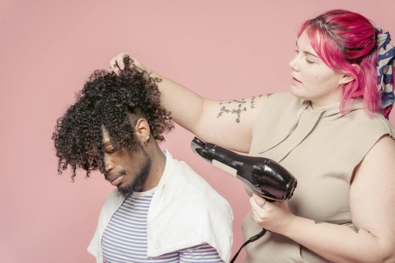 A hairstylist blow-dries a man's curly afro hair in a studio setting.
