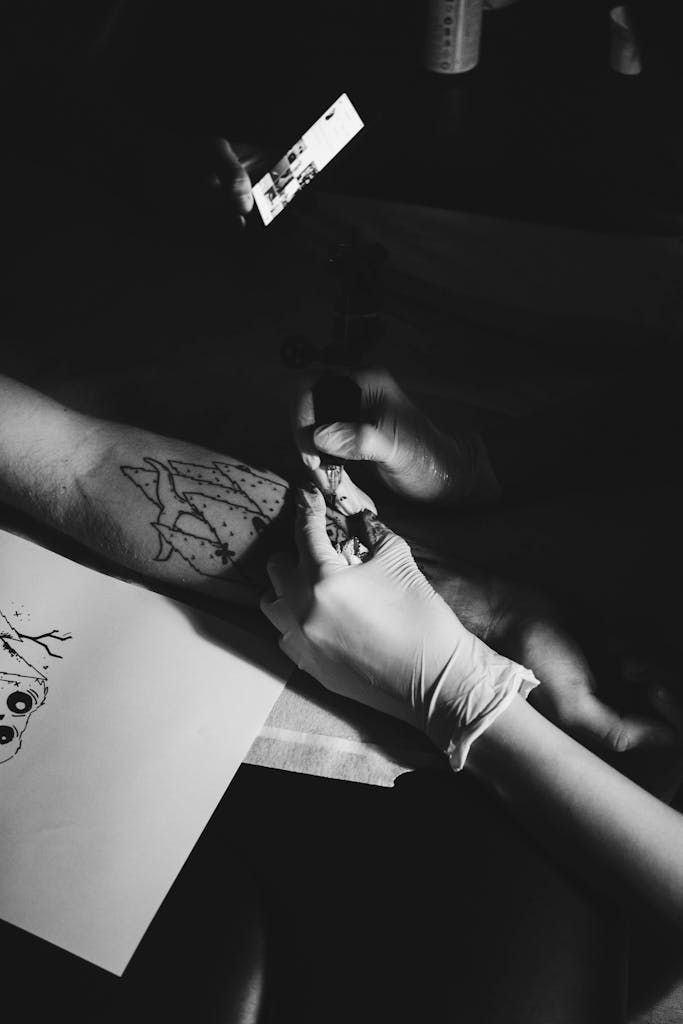Black and white image of a tattoo artist working on a client's arm.